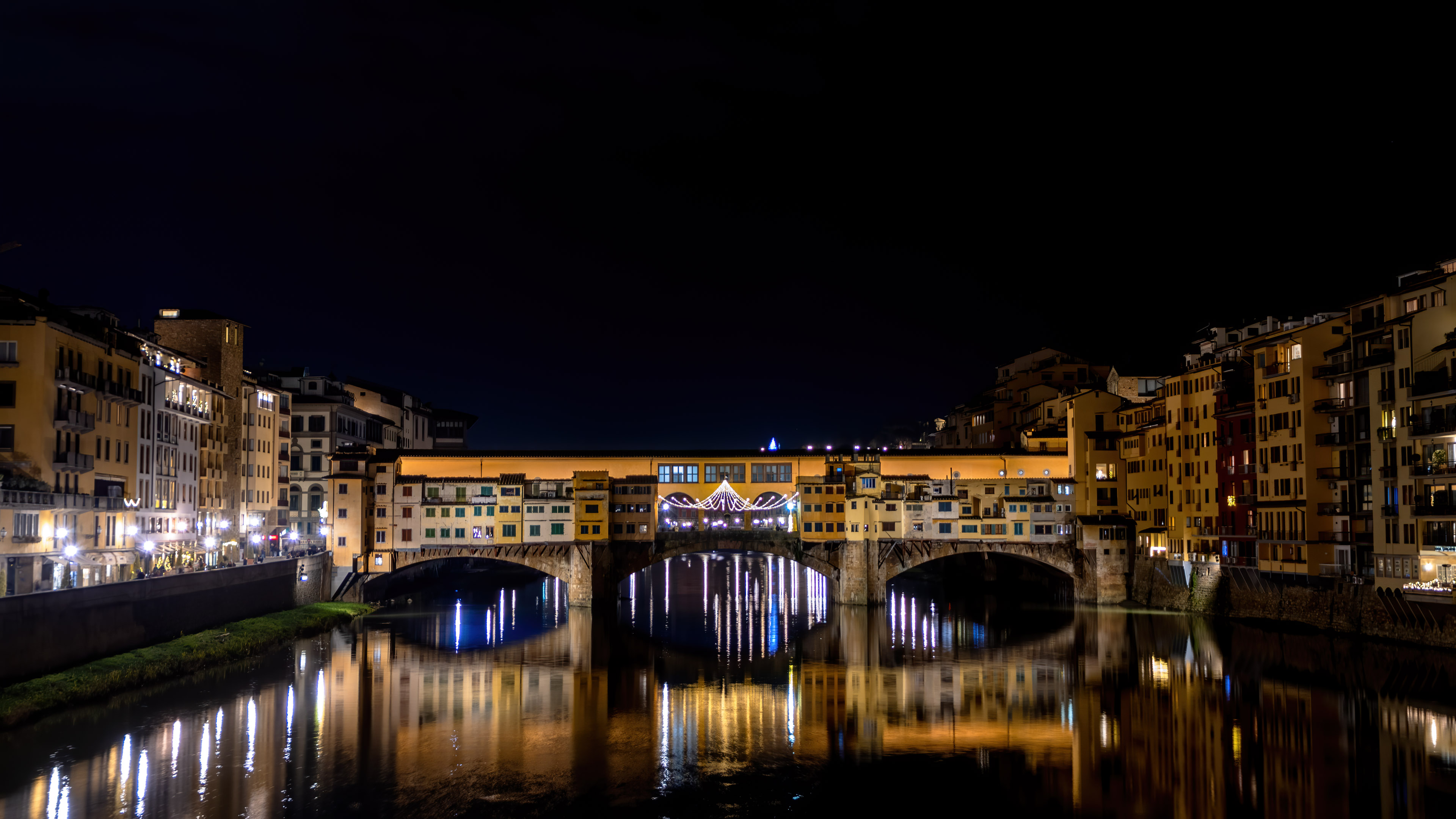 Experience the beauty of Florence at night with this stunning city wallpaper showing illuminated buildings and bridges.