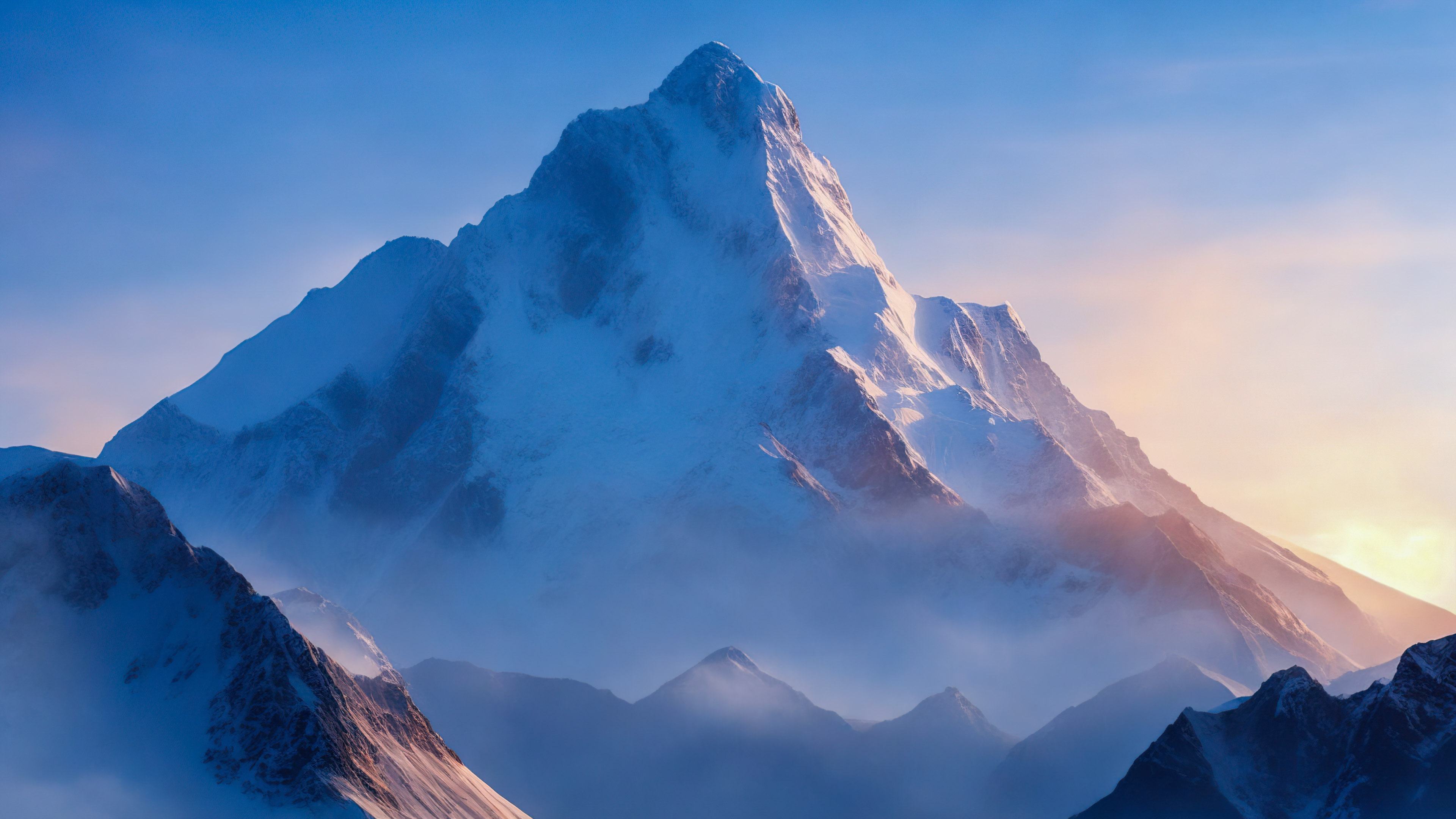 Faites l'expérience de la grandeur de notre fond d'écran 4k de beaux paysages, présentant un sommet de montagne pittoresque embrassé par la première lumière de l'aube sous un ciel bleu pâle.