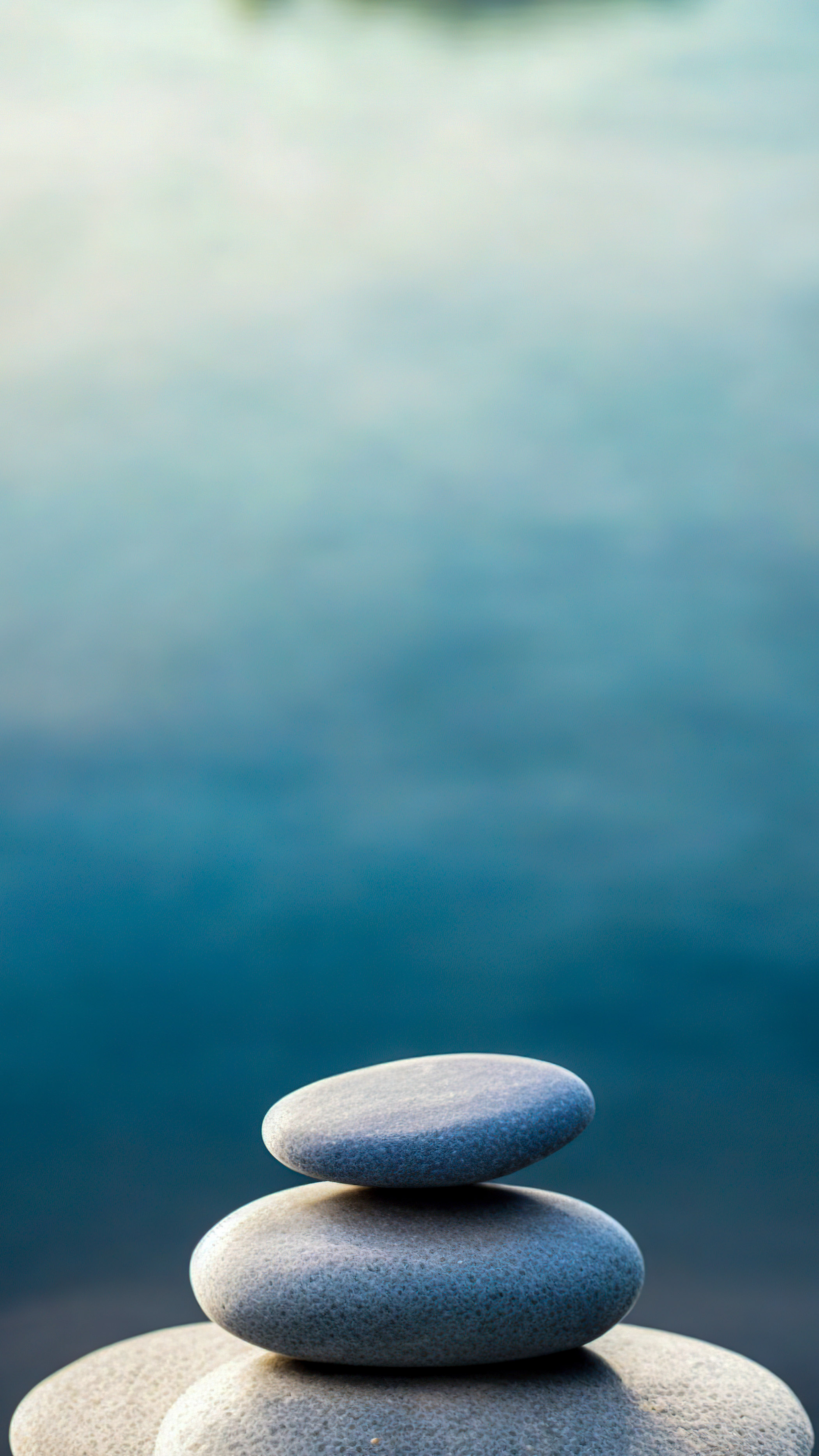 Expérimentez le minimalisme à son meilleur avec notre fond d'écran iPhone HD style, un design minimaliste mettant en vedette des pierres Zen empilées contre un fond d'eau serein.