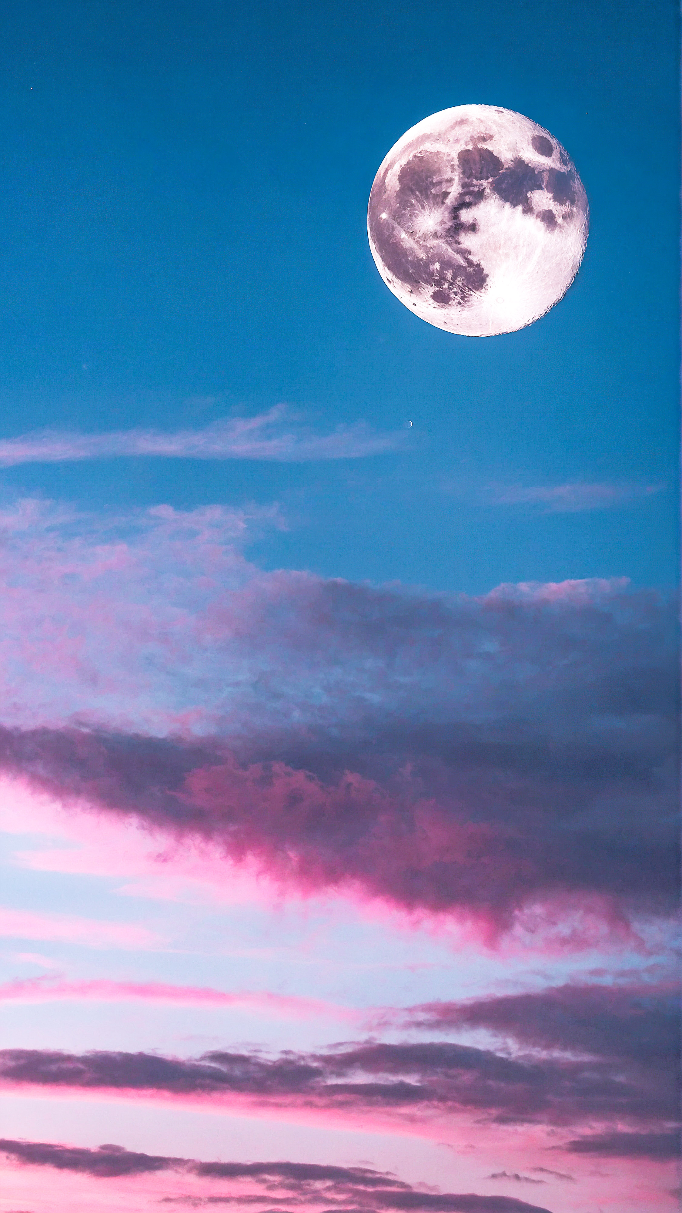 Expérimentez la tranquillité d'un ciel passant du bleu au rose avec des nuages duveteux et une pleine lune claire avec notre économiseur d'écran mignon pour iPhone.