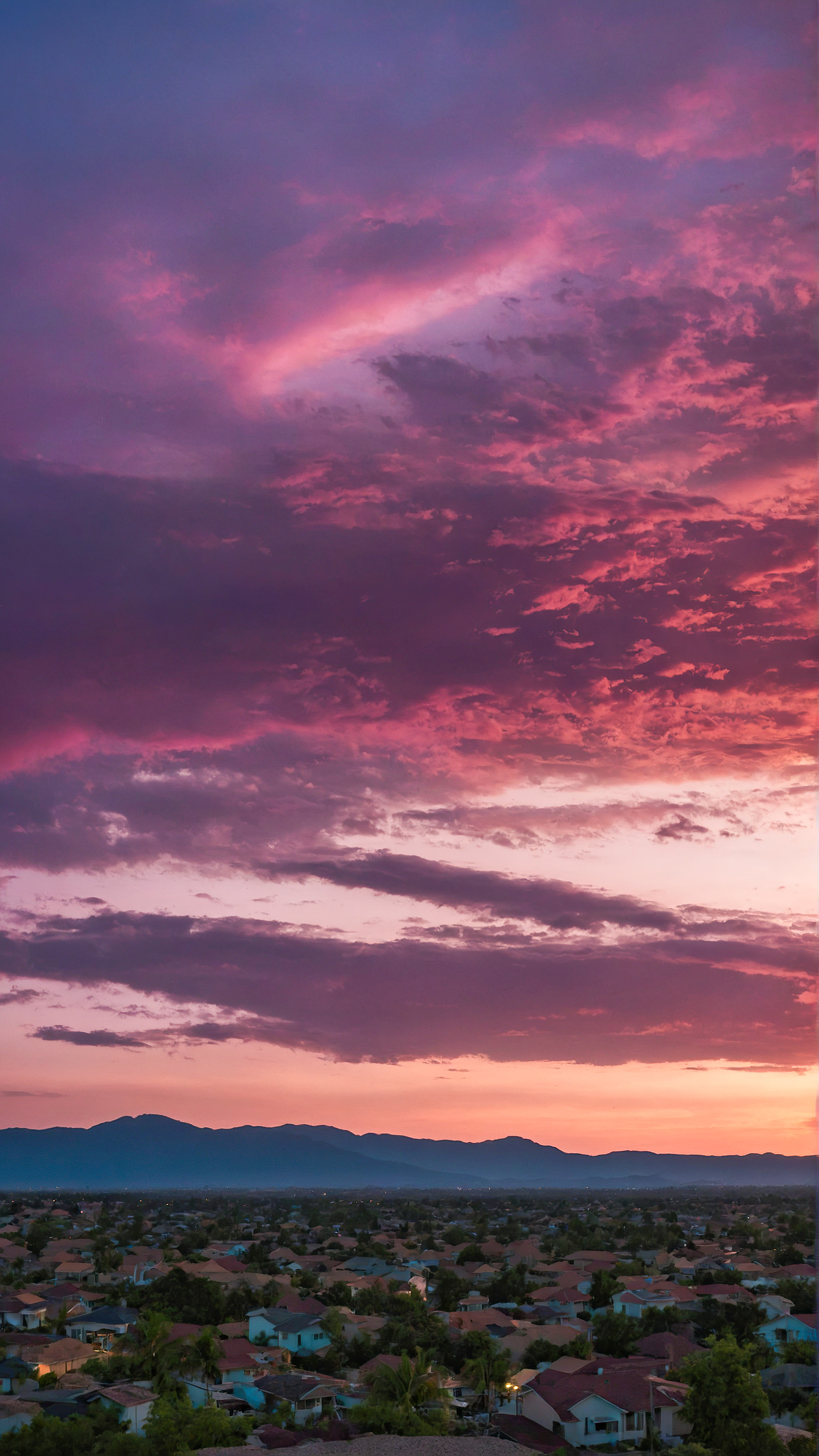 Experience the tranquility of a serene and colorful evening sky transitioning from deep purple to warm pink over the silhouette of a quiet town with our cute aesthetic backgrounds for iPhone.