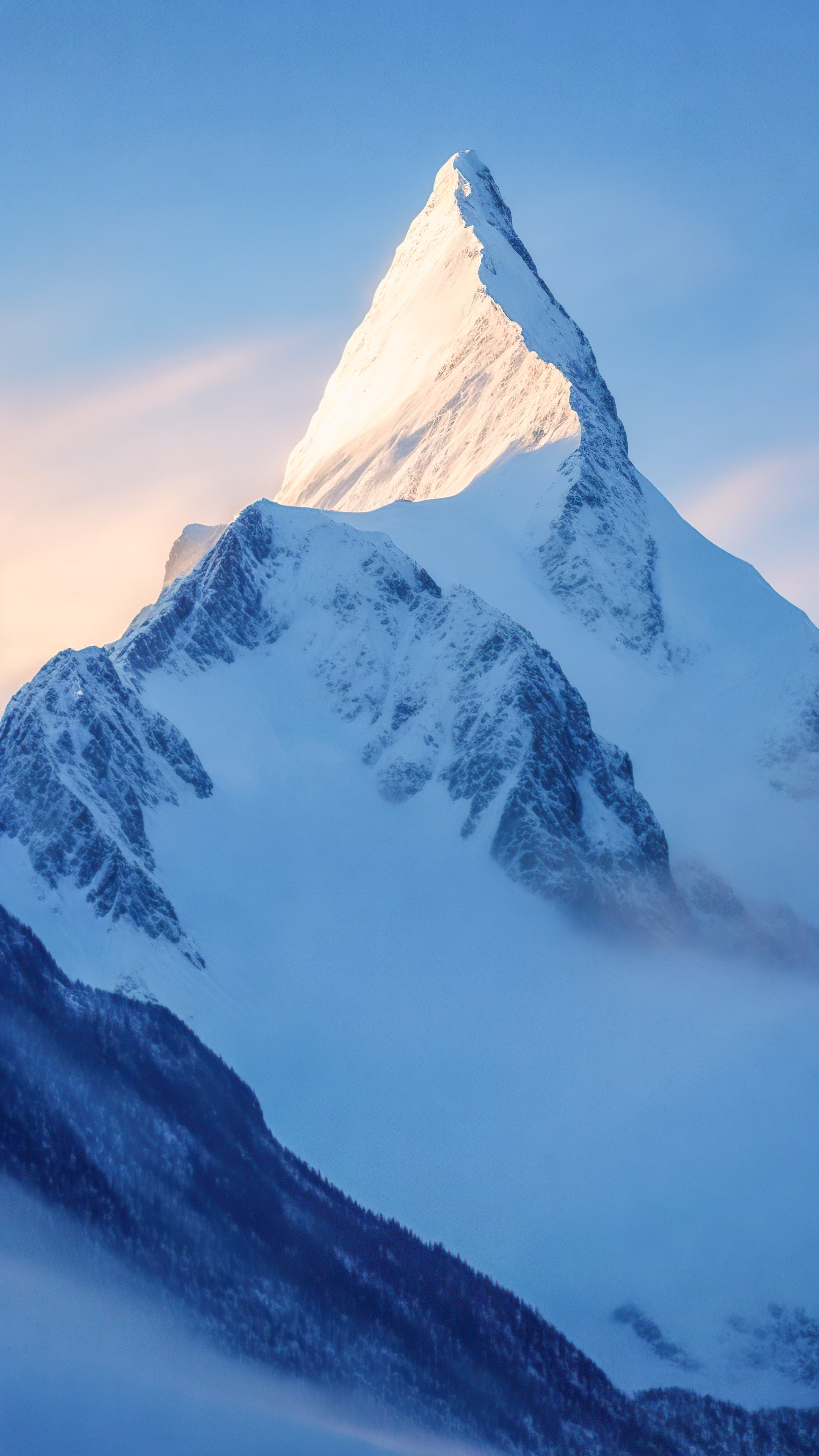 Capturez l'essence d'un pittoresque sommet de montagne embrassé par la première lumière de l'aube sous un ciel bleu pâle avec nos fonds d’écran de montagne en 4K pour votre iPhone.