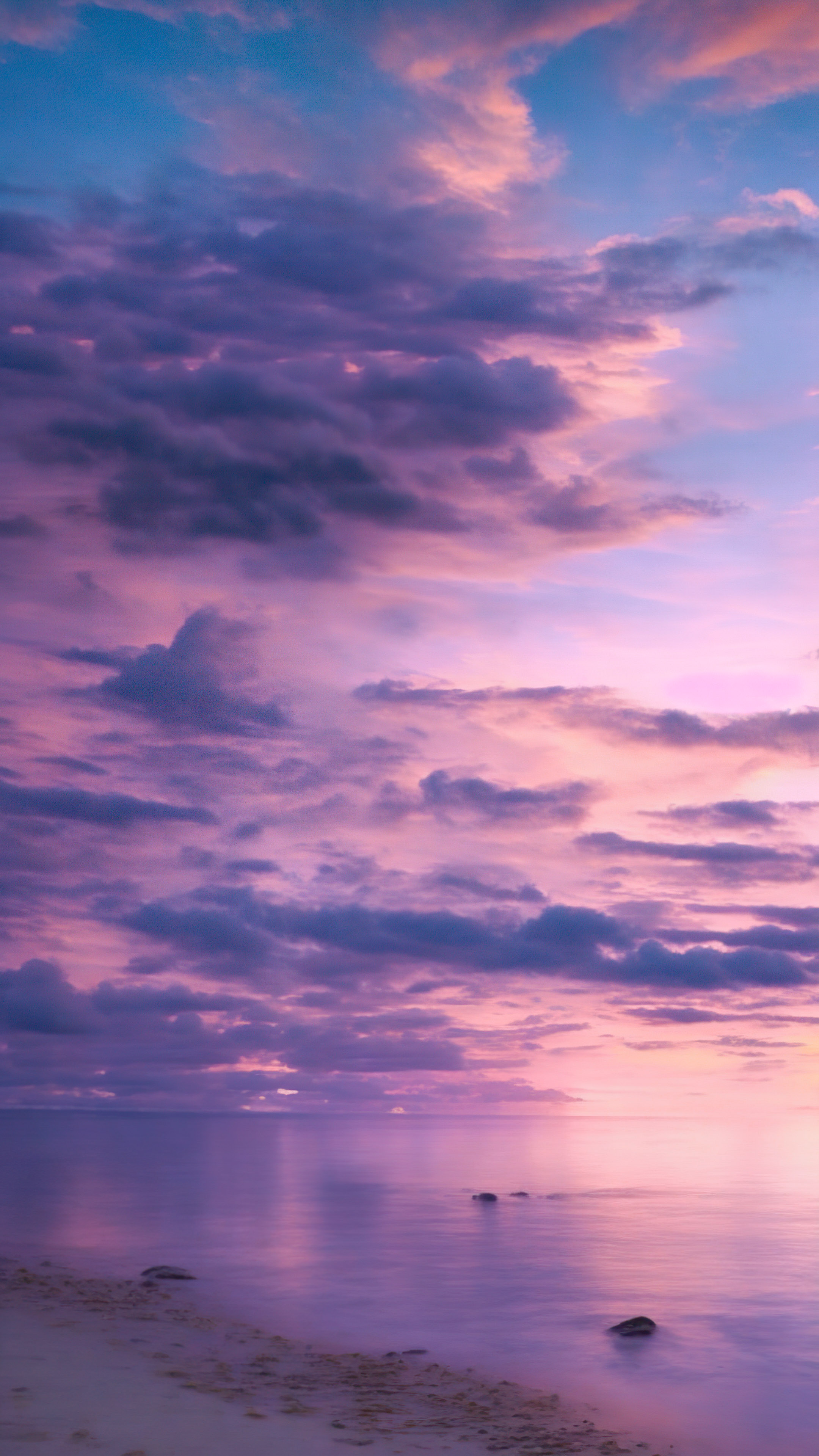 Admire the elegance of a tranquil beach at twilight, with the sky painted in shades of purple and pink, with pretty purple clouds wallpaper.